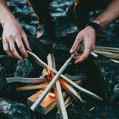 ian-keefe-yPBHXvN3HII-unsplash een man die een vuur opbouwt door hout toe te voegen